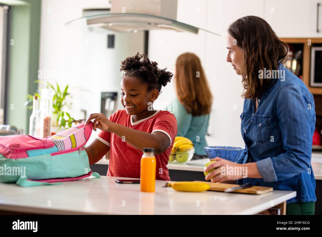 Donna caucasica matura guardando african american ragazza imballaggio borsa scuola a tavola Foto Stock