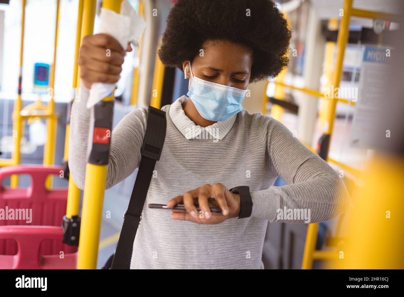 Donna d'affari afroamericana di metà adulto che indossa maschera controllo tempo mentre in piedi in autobus Foto Stock
