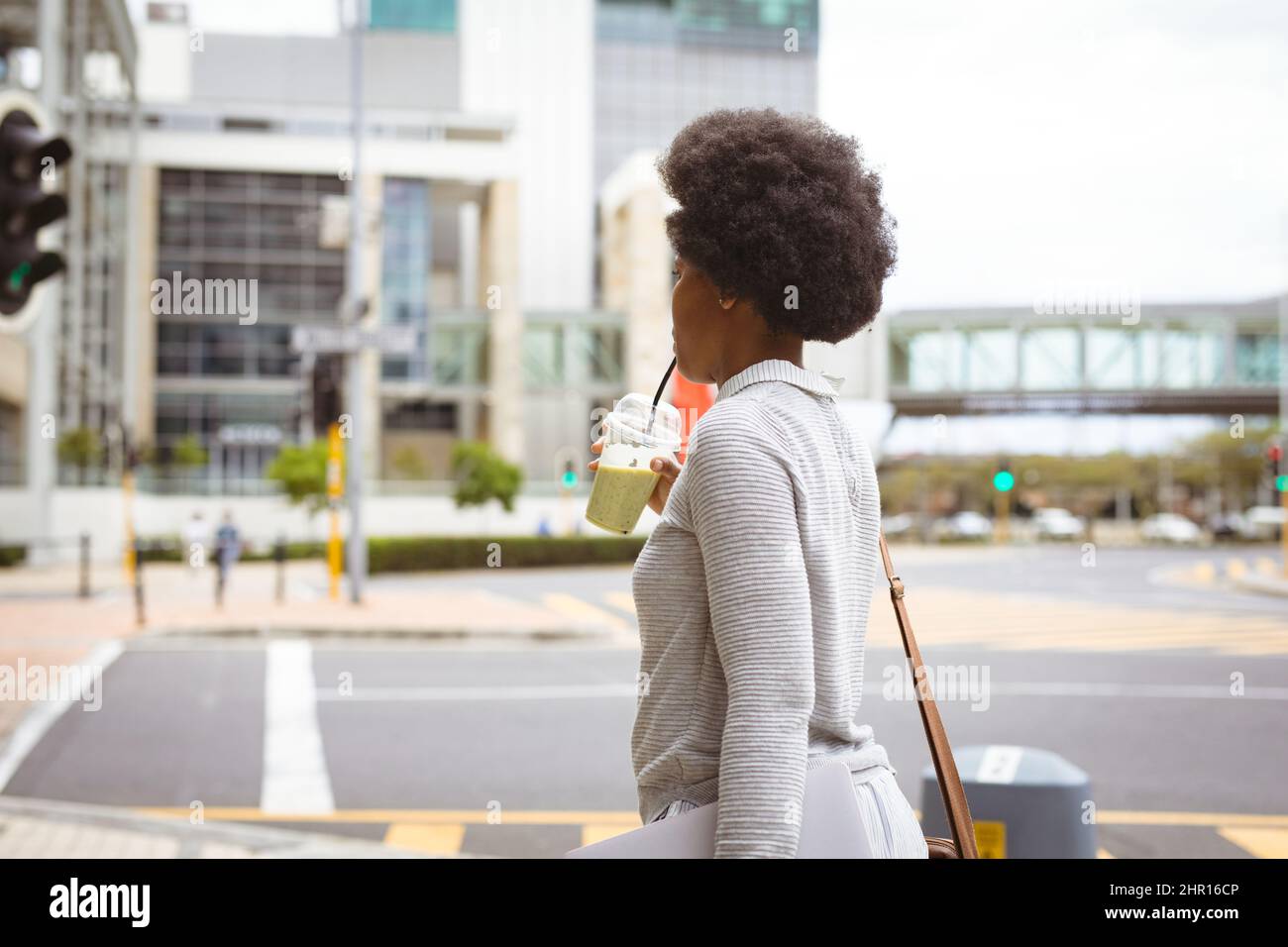 Donna d'affari afroamericana di metà adulto che beve mentre cammina sulla strada in città Foto Stock