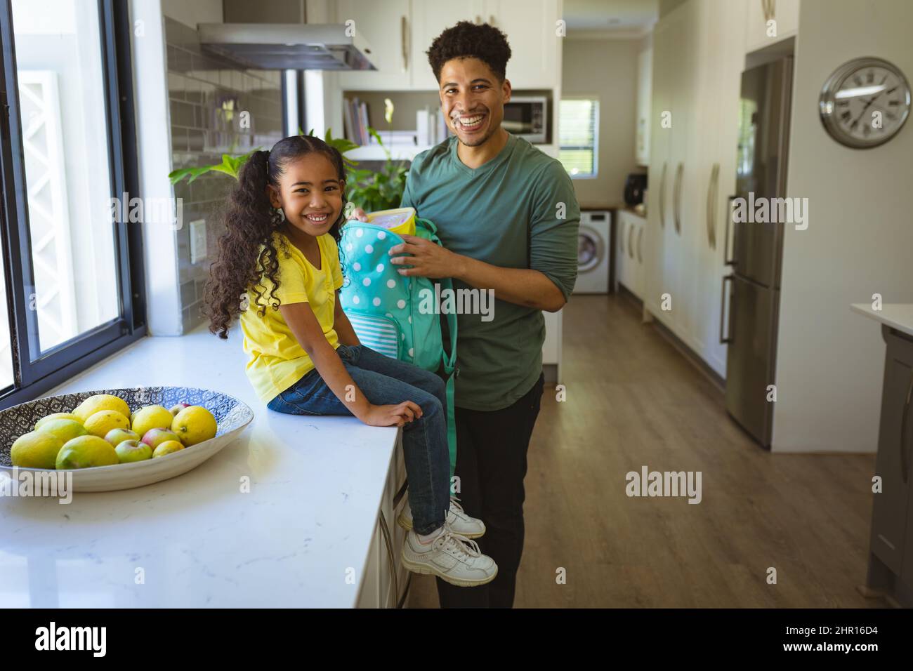 Ritratto di padre e figlia biraciale sorridente con zaino in cucina a casa Foto Stock