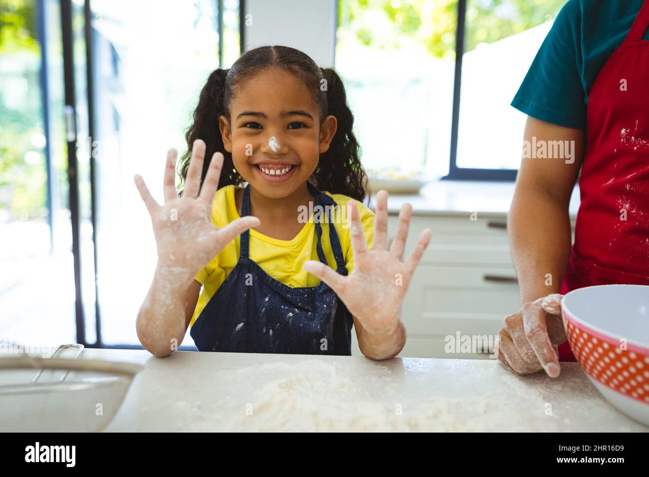 Ritratto di ragazza biraciale felice carino mostrando le mani sudicie coperte di farina da padre in cucina Foto Stock