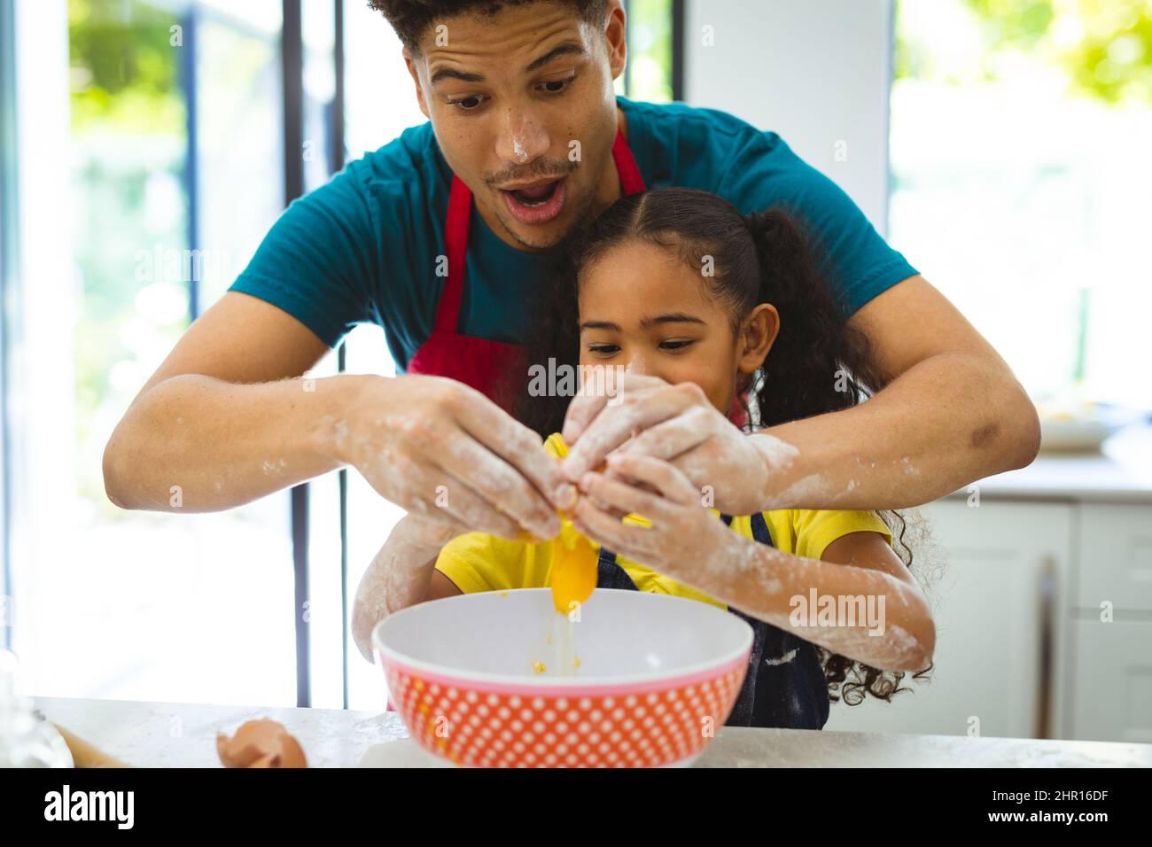 Il padre biraciale insegna la cottura della figlia mentre rompono l'uovo nella ciotola al banco della cucina Foto Stock