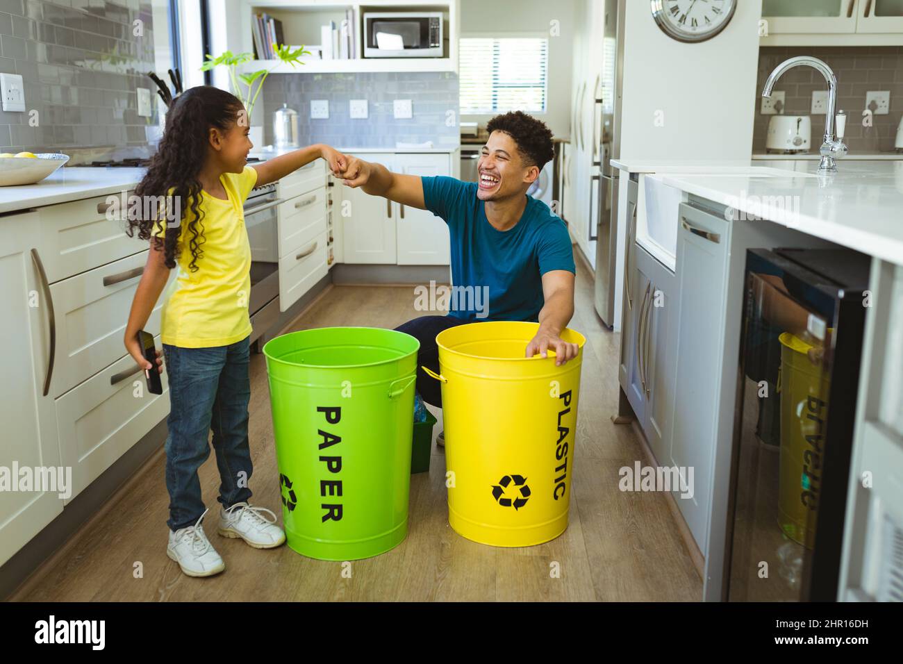 Felice padre e figlia multirazziale dando il pugno bump mentre facendo gestione dei rifiuti in cucina Foto Stock