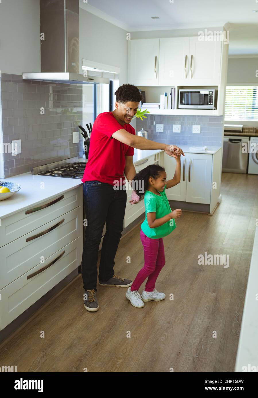 Sorridendo l'uomo biraciale che gira la figlia mentre si divergono insieme in cucina a casa Foto Stock