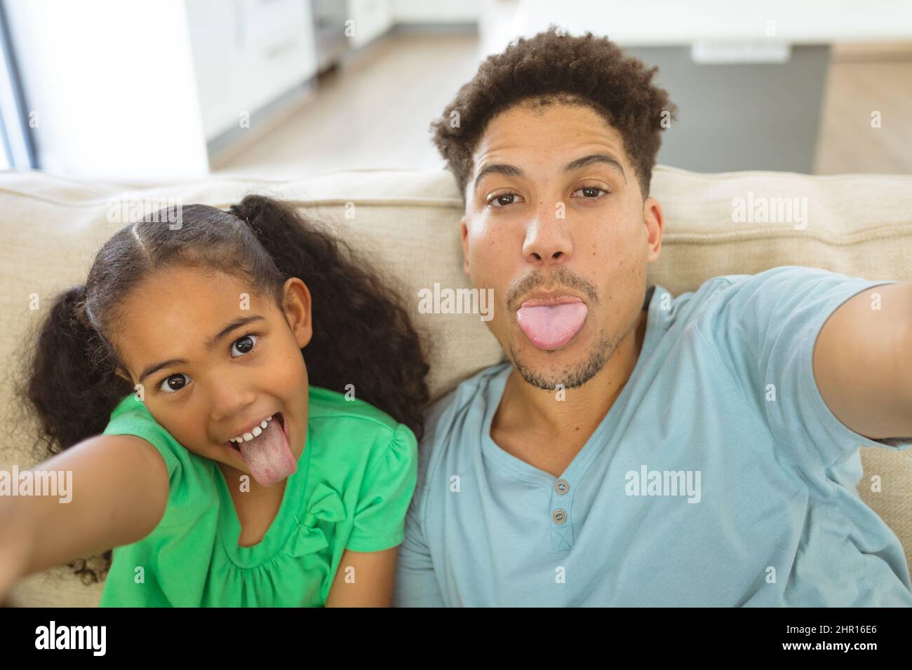 Divertente padre e figlia biraciale che prende selfie mentre si aggira la lingua a casa Foto Stock