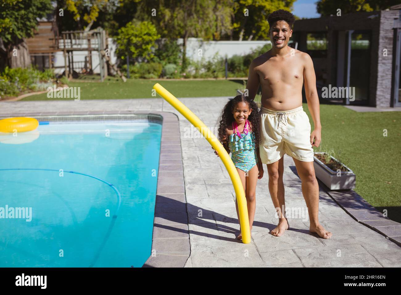 Ritratto di padre e figlia multirazziale sorridente che tiene galleggiante a bordo piscina Foto Stock