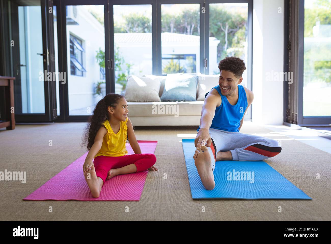 Sorridente padre e figlia multirazziale che praticano lo yoga insieme sui tappetini nel soggiorno in camera Foto Stock