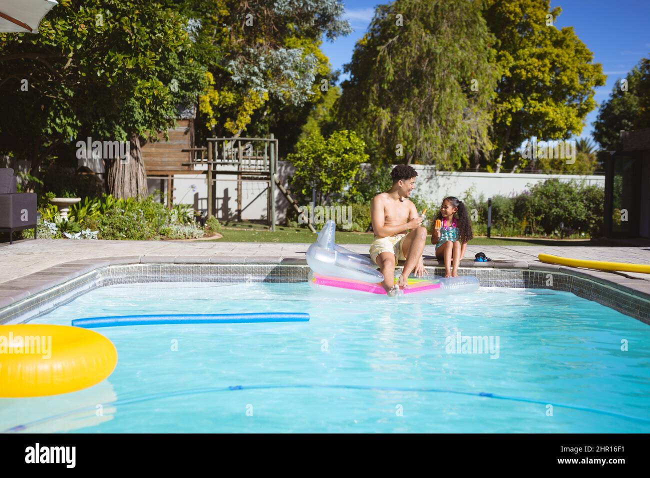 Padre e figlia multirazziale seduti a bordo piscina in cortile il giorno di sole Foto Stock