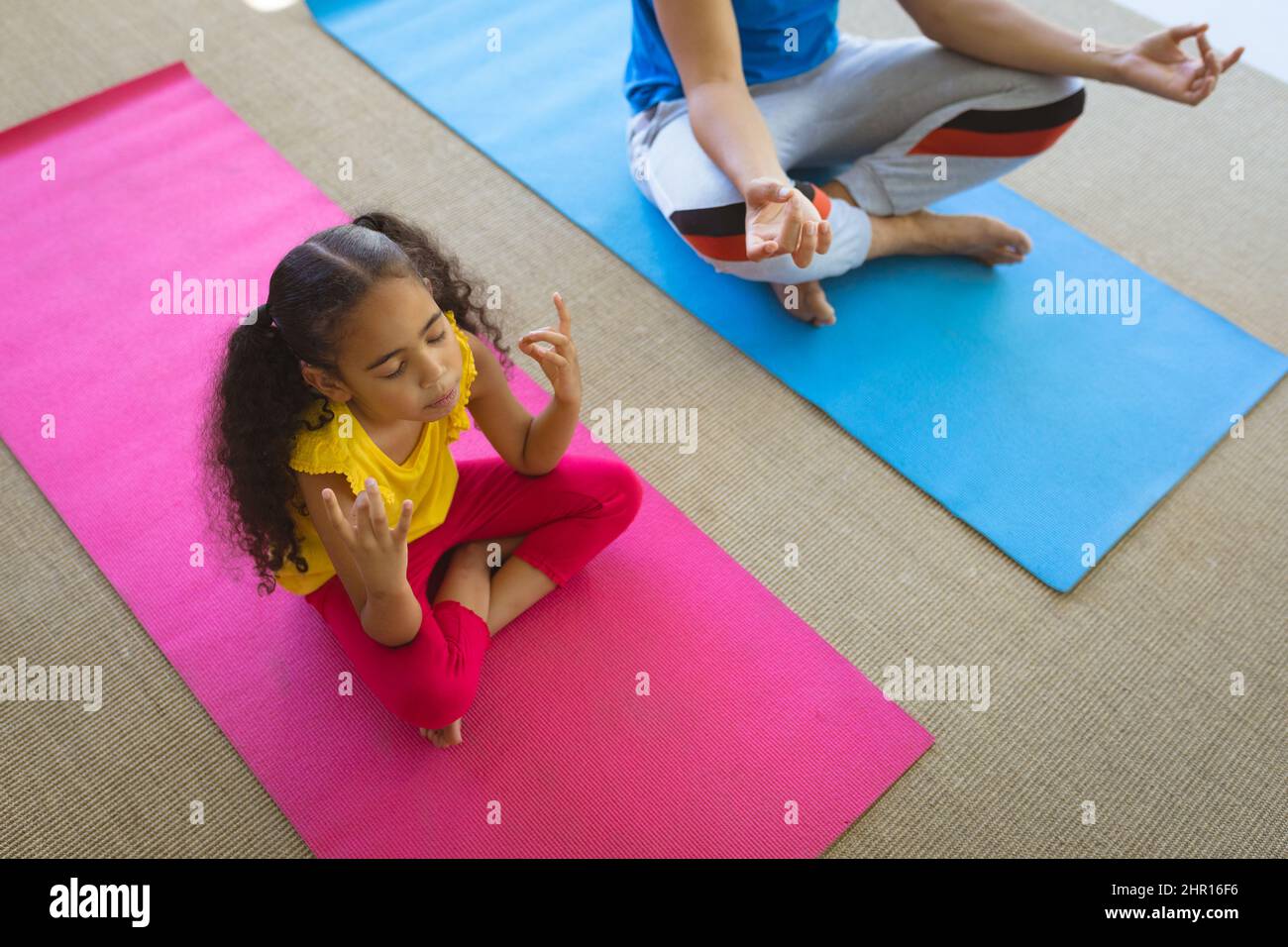 Vista ad alto angolo della ragazza biraciale che pratica yoga mentre meditando con il padre sui tappetini a casa Foto Stock