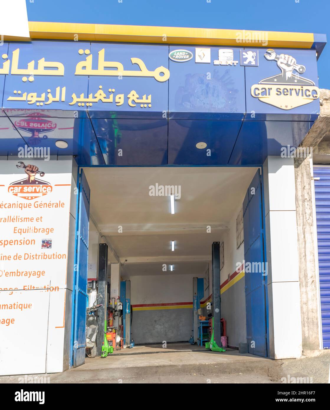 Garage di servizio auto vuoto per la riparazione di veicoli con i marchi delle aziende, targhetta in arabo, inglese e francese. Logo di una mano che tiene una chiave. Foto Stock
