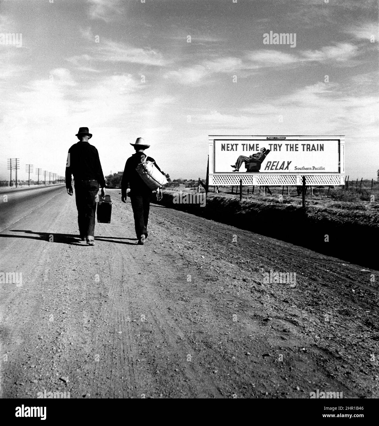 Dorothea Lange - sulla strada per Los Angeles - due uomini sulla strada passano il cartellone ironico che esalta le virtù del viaggio in treno, come se - Marzo, 1937. Foto Stock