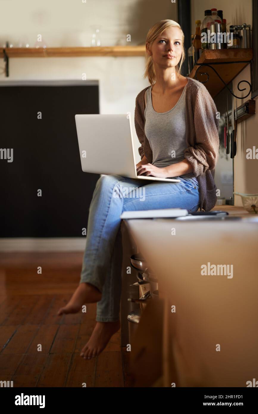 Scottando un paio di idee di ricetta.... Scatto di una giovane donna attraente che usa il suo laptop mentre si rilassa a casa. Foto Stock