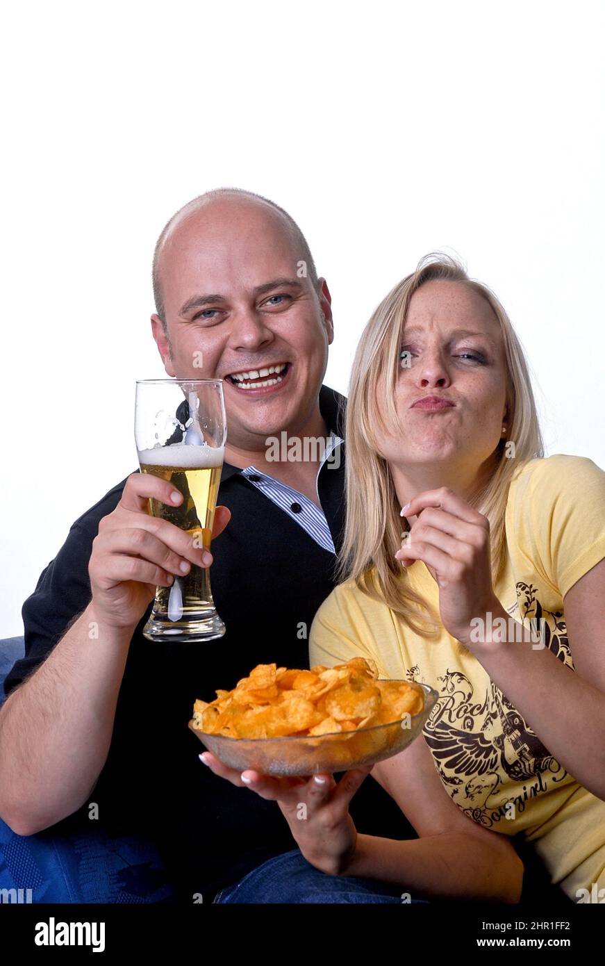 La coppia gode di una serata accogliente guardando la TV con una ciotola di patatine e un bicchiere di birra Foto Stock