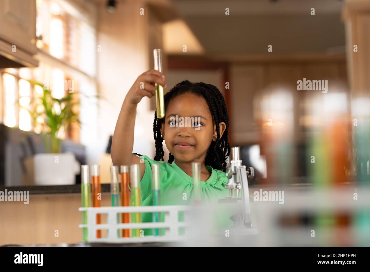 Cute innocente ragazza afroamericana che esamina la soluzione in provetta a casa Foto Stock