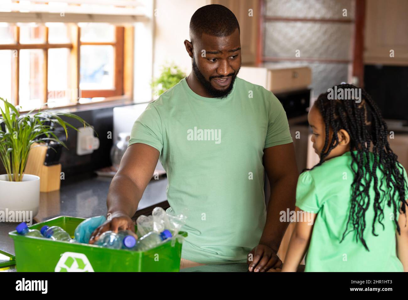 Uomo afroamericano che insegna a riciclare bottiglie di plastica in cucina a casa Foto Stock