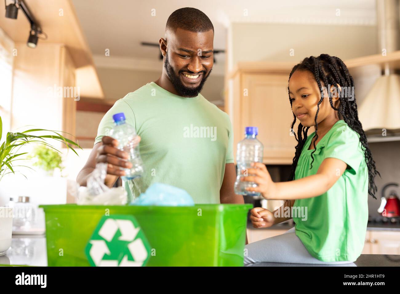 Felice padre e figlia afroamericana che mette le bottiglie in contenitore di riciclaggio a casa Foto Stock