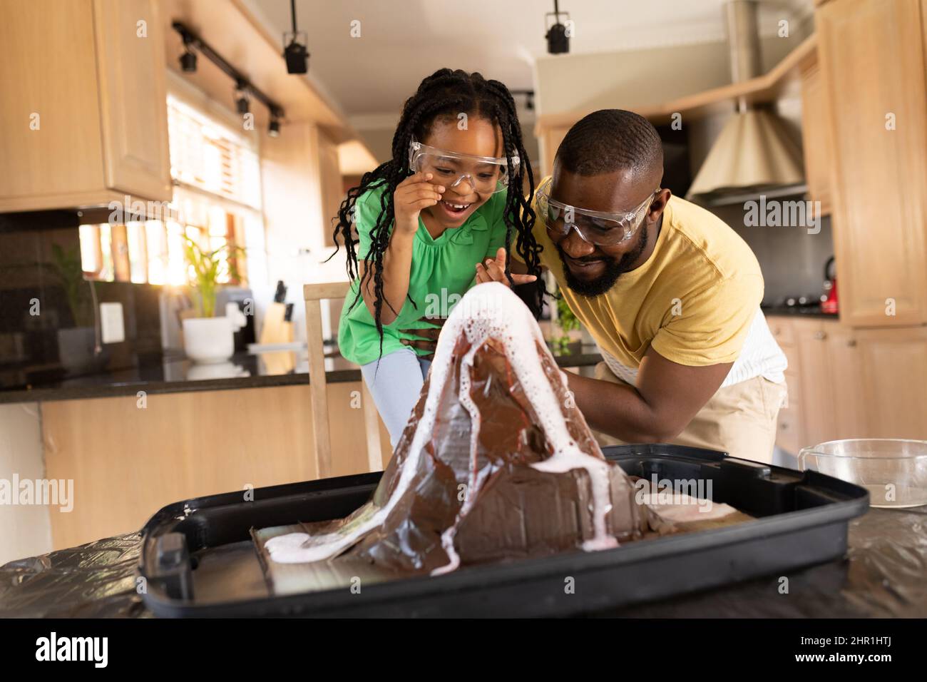 Stupito ragazza afroamericana con padre che esamina esperimento scientifico in cucina a casa Foto Stock