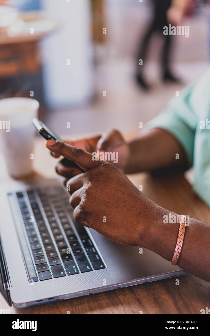 primo piano delle mani dell'uomo usando il telefono delle cellule con il laptop ed il caffè Foto Stock