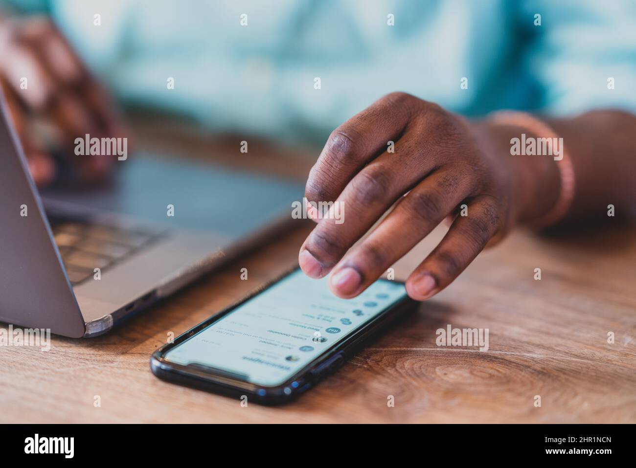 primo piano delle mani dell'uomo nero con il portatile e scorrimento sul telefono Foto Stock