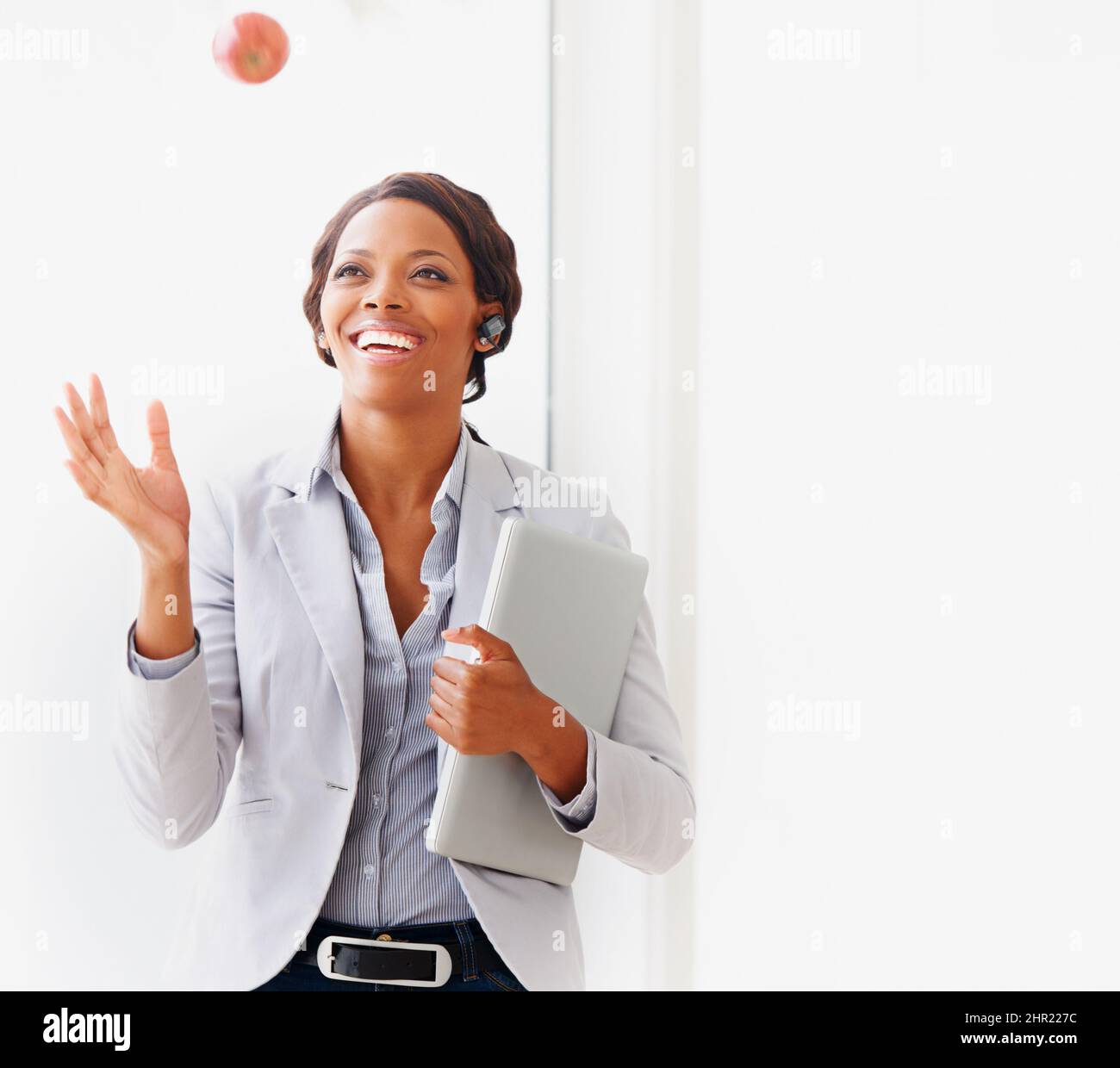 Salute e affari vanno di pari passo per lei. Una giovane donna d'affari afroamericana che lancia una mela nell'aria. Foto Stock