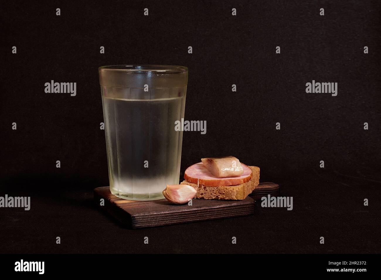 Bicchiere sfaccettato di vodka, panino con pane di segale, aringhe, prosciutto, spicchi d'aglio Foto Stock