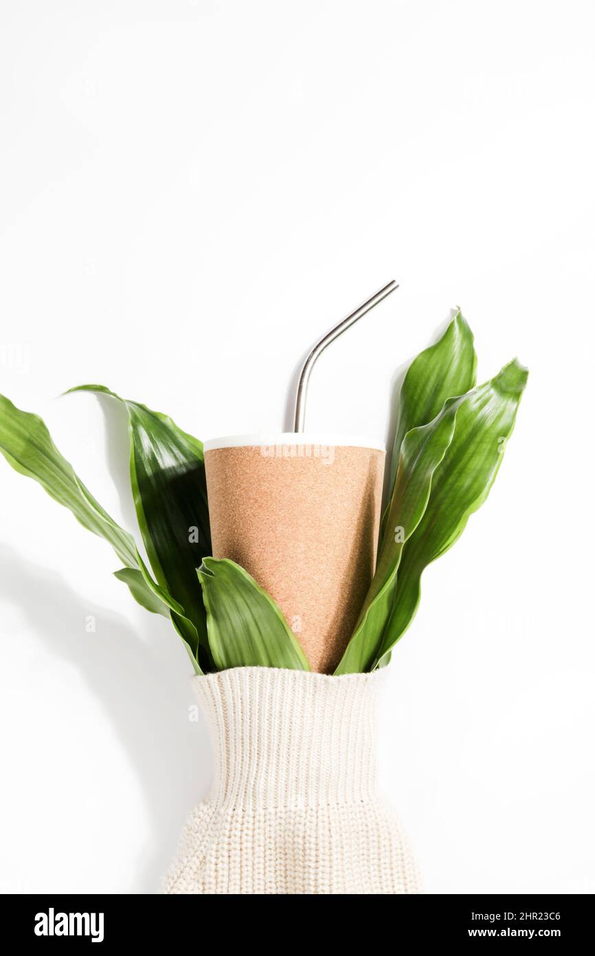 tazza ecologica riutilizzabile e rami di pianta in manica di maglione su sfondo bianco. Stile di vita sostenibile, consumo consapevole, concetto. Spazio di copia Foto Stock