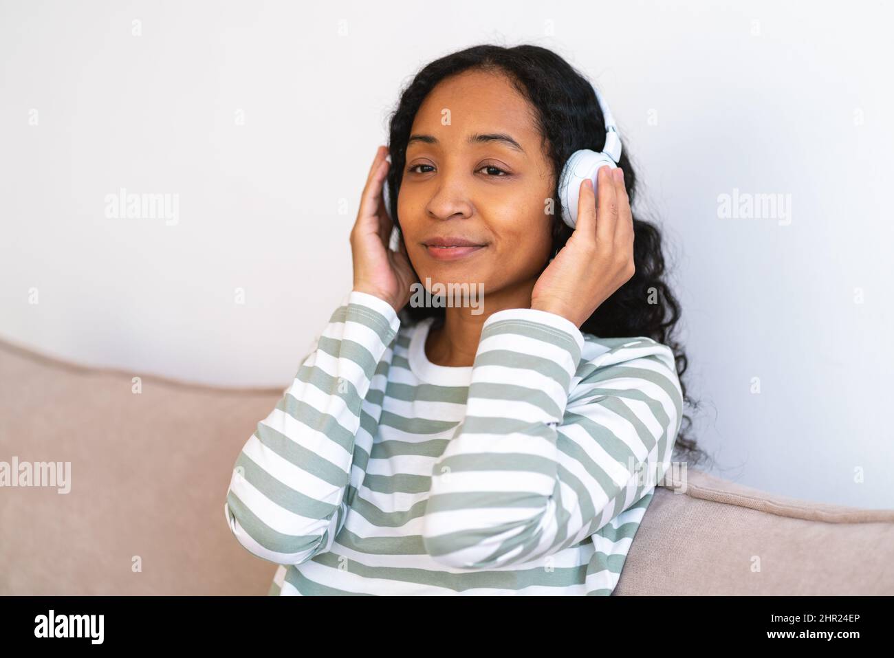 Ascoltare la musica con le cuffie. Deliziosa donna afroamericana che ascolta la sinfonia sul divano Foto Stock