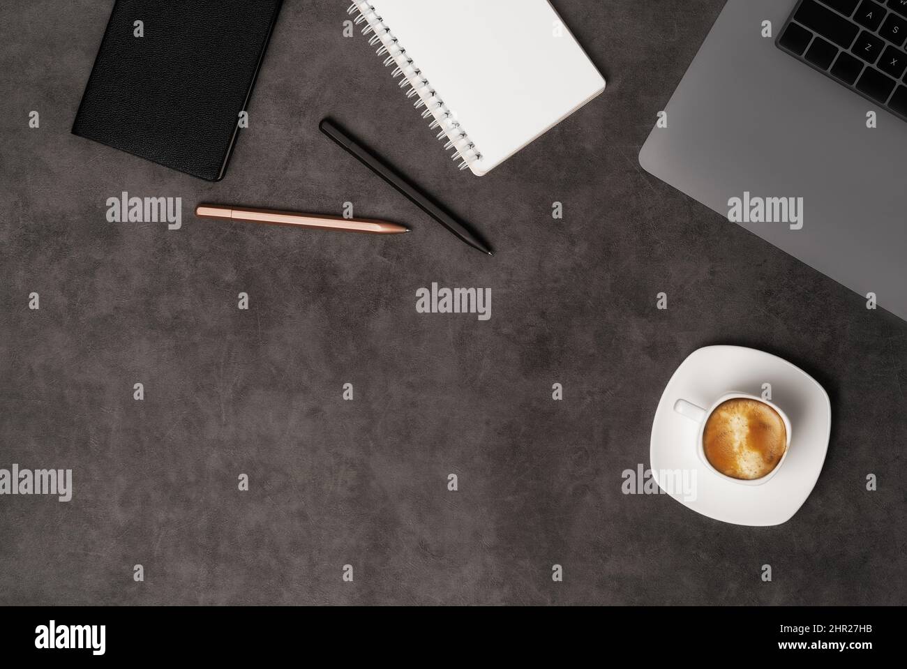 Vista dall'alto dell'area di lavoro con computer portatile, blocco note, penne e caffè su sfondo di pietra grigio scuro. Disposizione piatta con spazio di copia. Concetto aziendale. Foto Stock