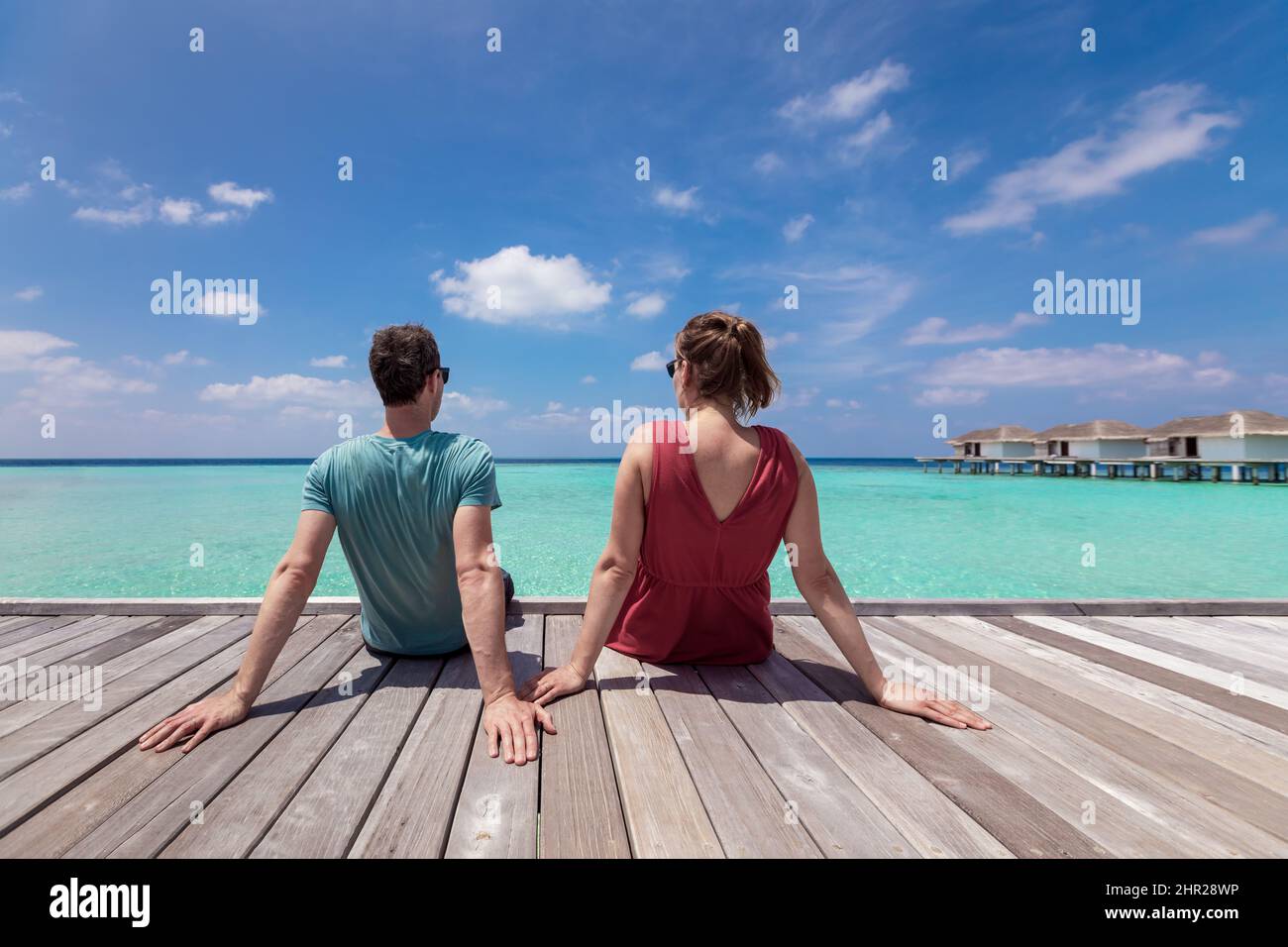 Coppia trascorrere romantiche vacanze in spiaggia in resort di lusso in Maldive con acque turchesi mare, cielo blu e ville sull'acqua seduta su WO Foto Stock