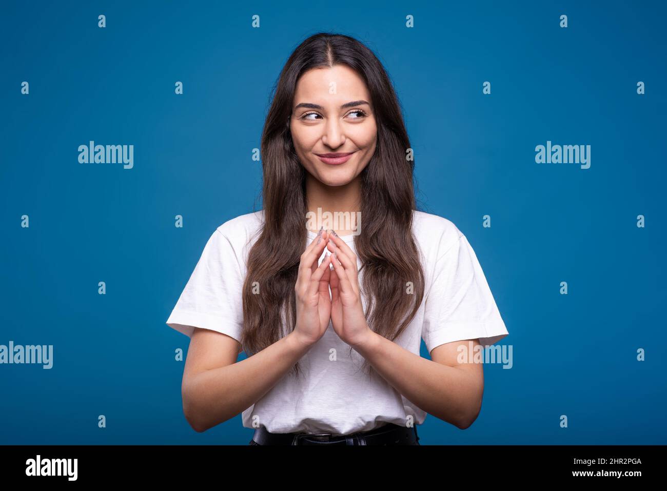 Attraente ragazza bruna caucasica o araba in una t-shirt bianca pensando e mostrando un gesto con le mani che sta tracciando un isolato di piano astuto Foto Stock