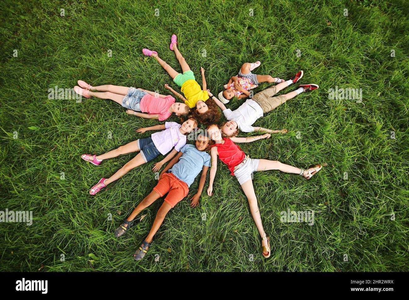 i bambini di razze e nazionalità diverse si trovano intorno sull'erba in abiti colorati e sorridono. Giorno dei bambini Foto Stock