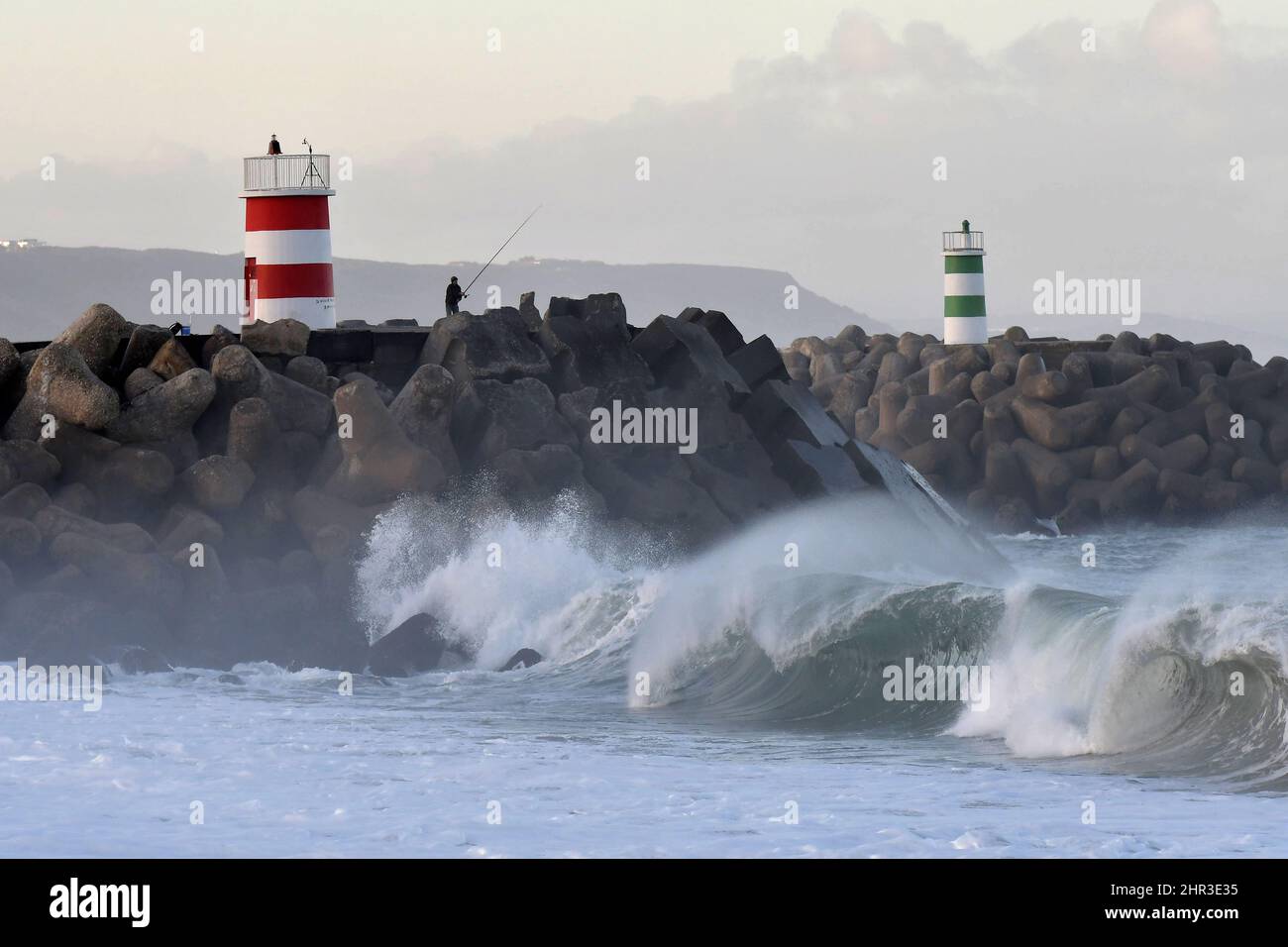 Pescatori su molo di pietra con fari, grandi onde che si infrangono sulla costa di Nazare in Portogallo. Foto Stock