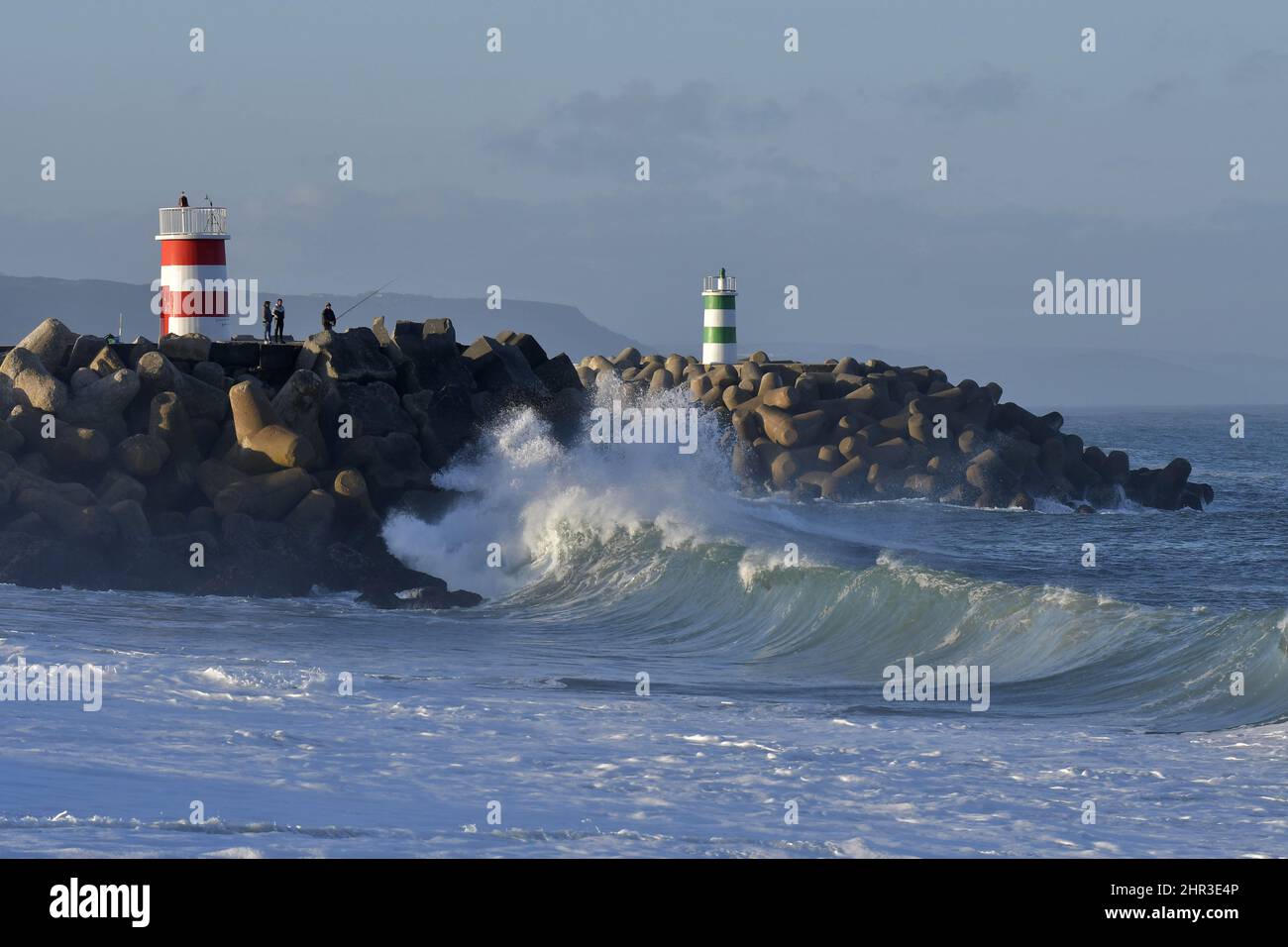 Pescatori su molo di pietra con fari, grandi onde che si infrangono sulla costa del Nazare Portogallo. Foto Stock