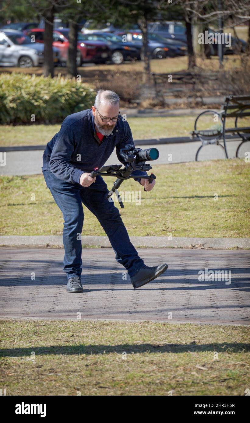 Un uomo che filma con una fotocamera. In un parco a Queens, New York, in una mite giornata invernale. Foto Stock Un uomo che filma con una fotocamera. In un parco a Queens, New York, in una mite giornata invernale. Foto Stock