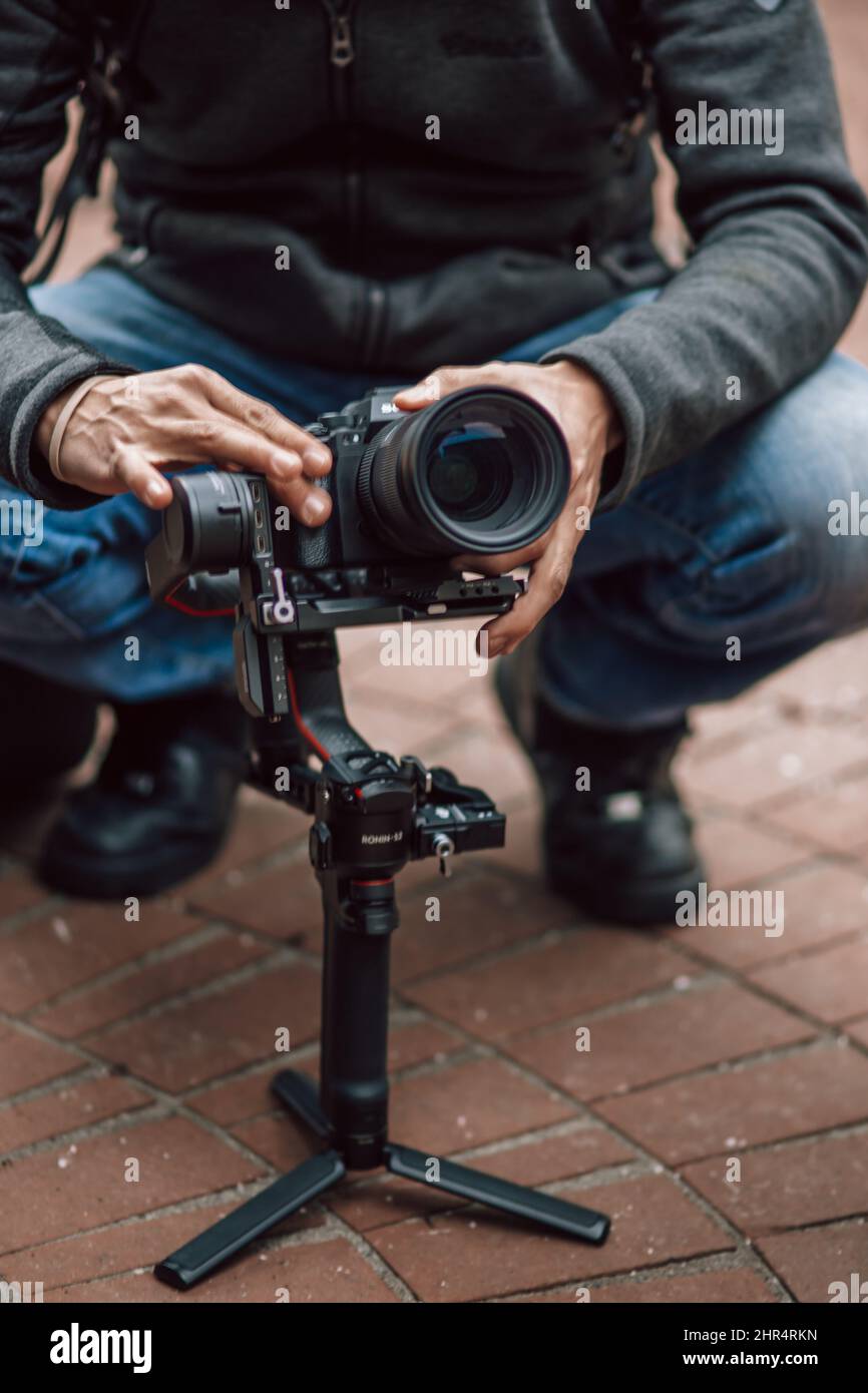 Fotografo che regola una fotocamera Sony DLSR Mirrorless montata su un gimbal Ronin S su un marciapiede Foto Stock