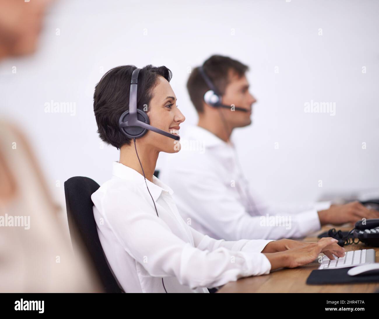 Felice di essere disponibile. Immagine di due operatori dell'help desk che indossano cuffie e lavorano al computer. Foto Stock