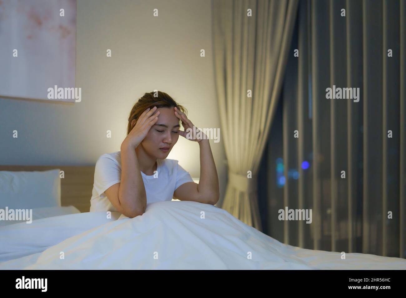 Donna asiatica sdraiata su un letto bianco in camera da letto che guarda preoccupata o pensa a qualcosa sulla sua vita o sul lavoro a metà notte a casa. Foto Stock