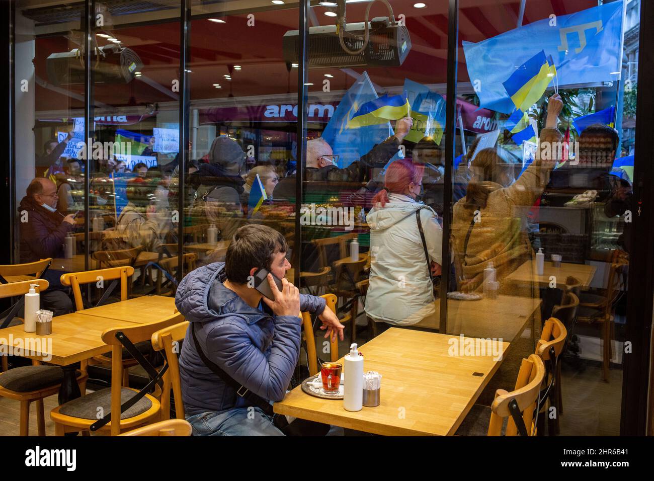 25 febbraio 2022: Un cliente seduto al ristorante è proprio accanto alla zona di protesta. Il secondo giorno delle proteste, i cittadini ucraini che vivono a Istanbul hanno condannato l'intervento russo in Ucraina con slogan e striscioni. I manifestanti, con bandiere e bandiere ucraine, si sono riuniti in via Istiklal e hanno cantato slogan contro Russia e Putin di fronte al Consolato Generale russo di Istanbul, Turchia, il 25 febbraio 2022. I manifestanti chiesero la fine della guerra. Anche i cittadini turchi hanno sostenuto la protesta. (Credit Image: © Tolga Ildun/ZUMA Press Wire) Foto Stock