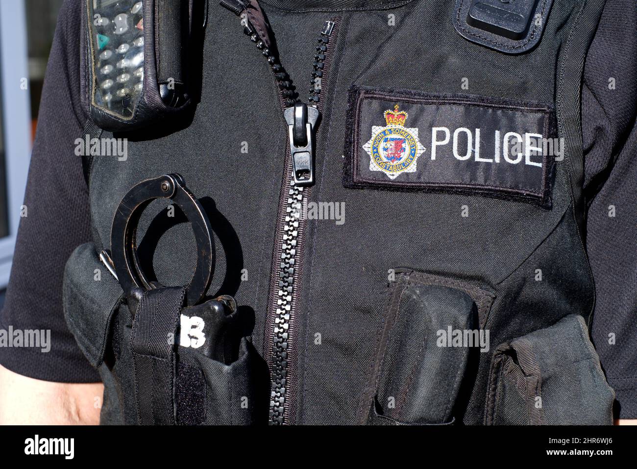 Un'immagine ravvicinata di una donna di poliziotti inglesi corazza o gilet di servizio equipaggiano con manette, radio personale, asp e insegne di polizia Foto Stock
