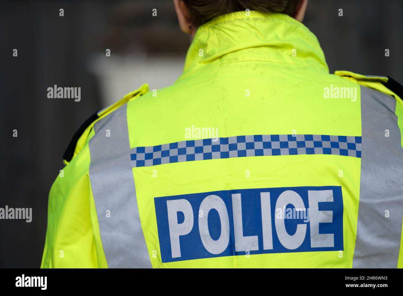 Un ufficiale di polizia femminile britannico che indossa una giacca riflettente ad alta visibilità. L'immagine mostra la parte posteriore dell'ufficiale e le indicazioni della polizia sono visibili Foto Stock