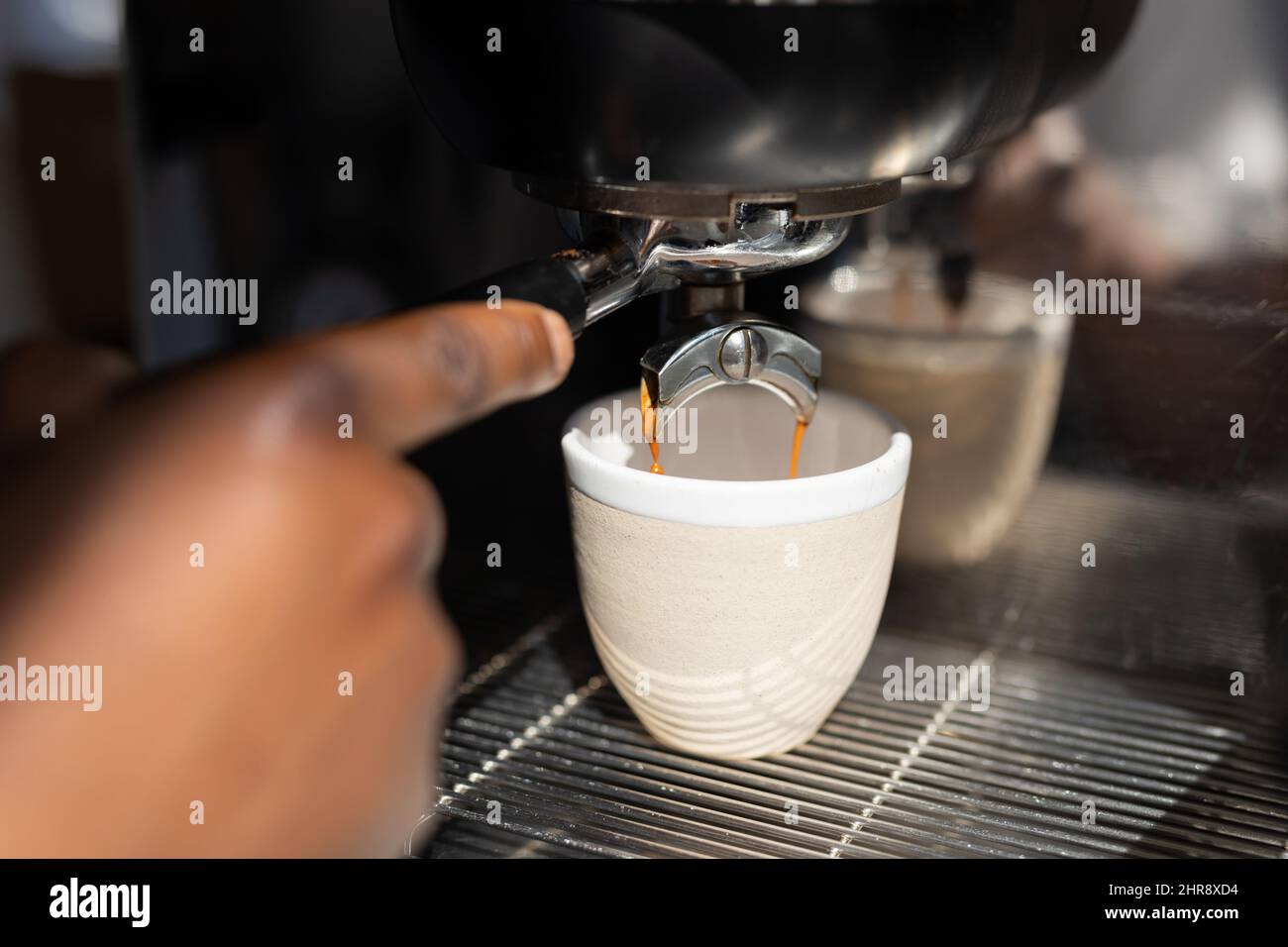 Mano tagliata di barista afroamericano che riempie la tazza con caffè fresco dalla macchina del caffè Foto Stock