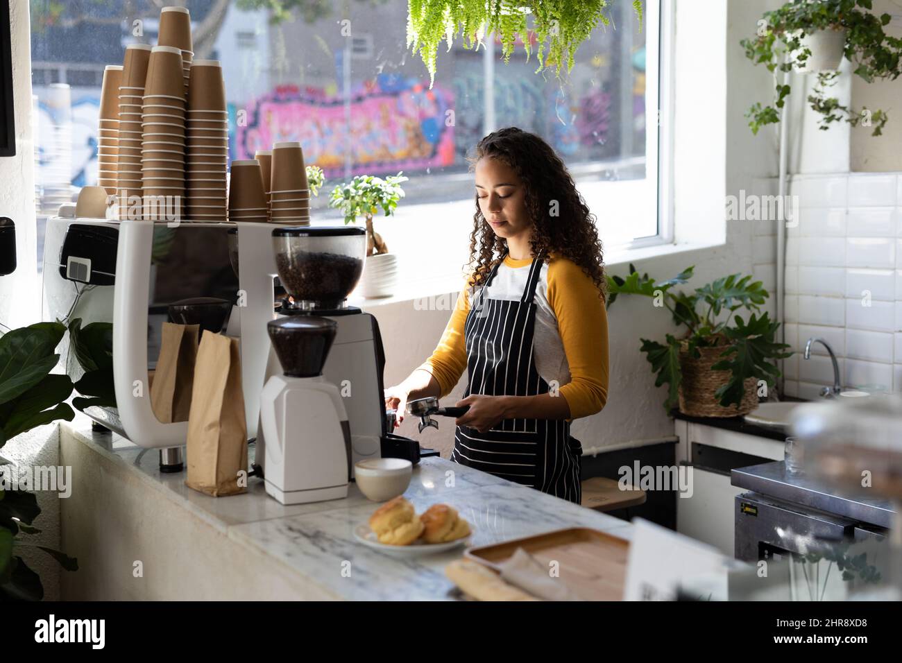 Giovane donna barista afroamericana che prepara il caffè dalla macchina al banco del caffè Foto Stock