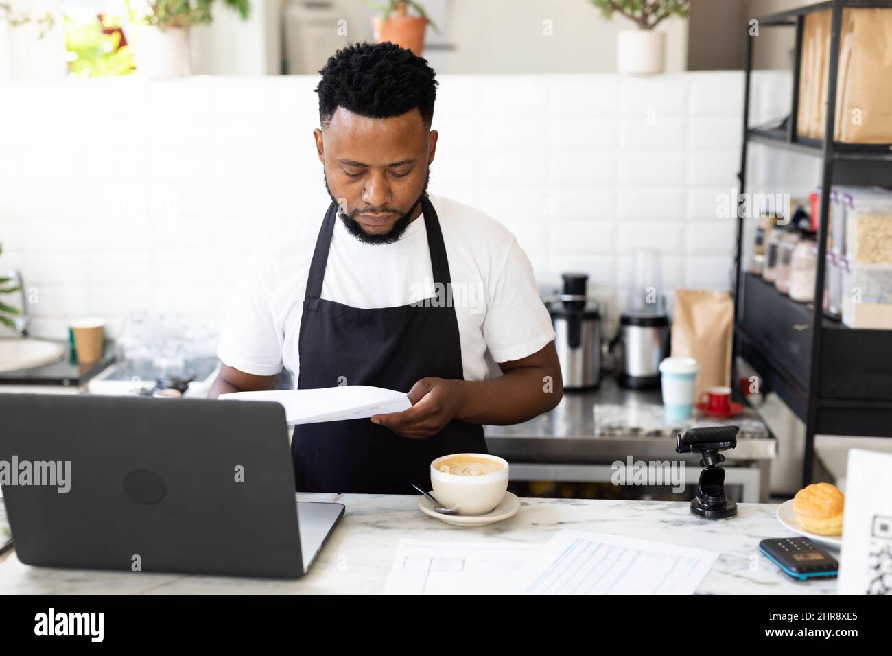 Giovane barista afroamericano maschile che prepara un caffè da computer portatile al banco del caffè Foto Stock