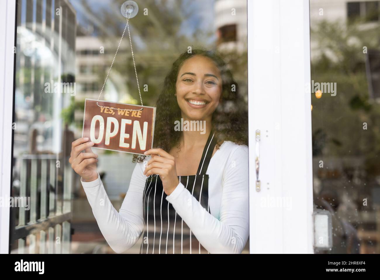 Sorridente barista afroamericano appeso un cartello aperto sulla porta di vetro nella caffetteria Foto Stock