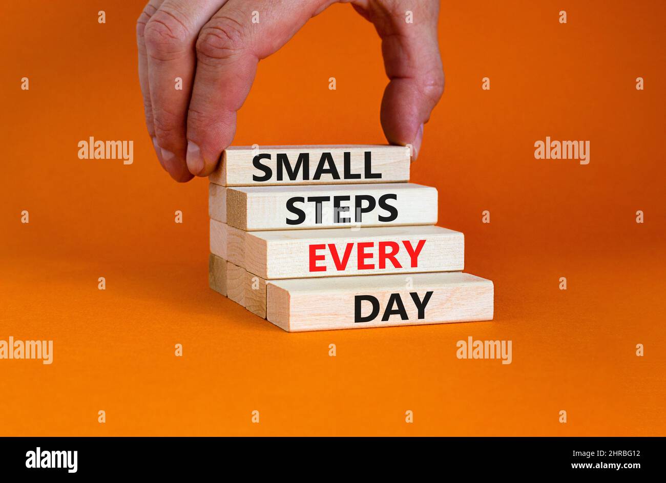 Simbolo piccoli passi ogni giorno. Parole di concetto piccoli passi ogni giorno su blocchi di legno. Mano dell'uomo d'affari. Bella tabella arancione sfondo arancione. Piccola Foto Stock