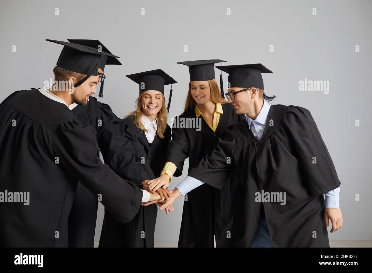 Gruppo di studenti universitari felici in berretti e camici che si divertono alla loro laurea Foto Stock