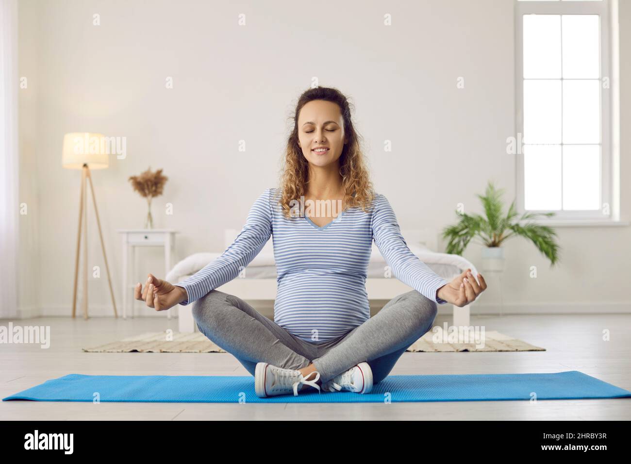 Donna incinta medita pratica yoga a casa Foto Stock