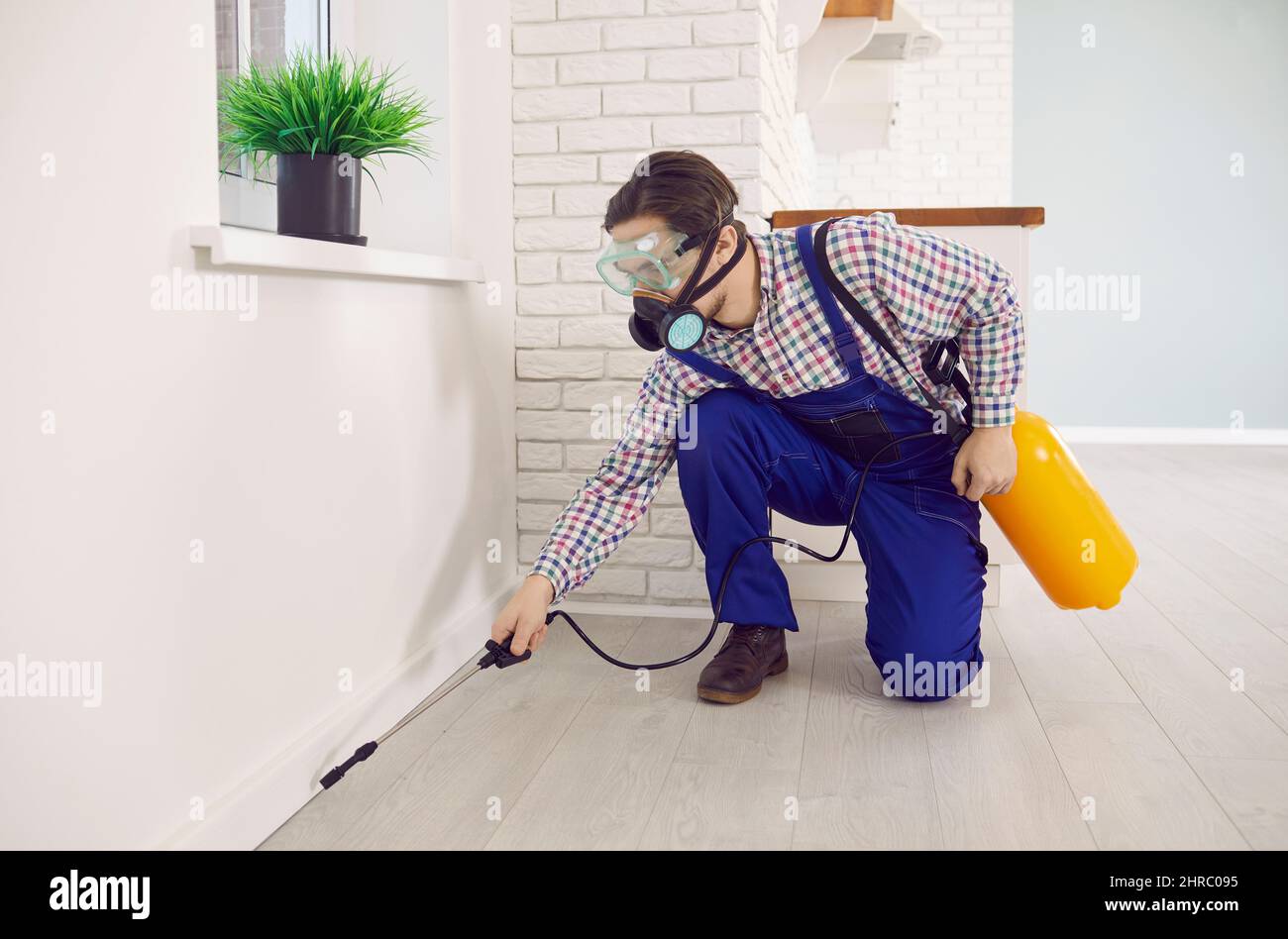 Il lavoratore di controllo di peste in una maschera e nell'abbigliamento da lavoro generale spruzzando veleno all'interno della casa Foto Stock