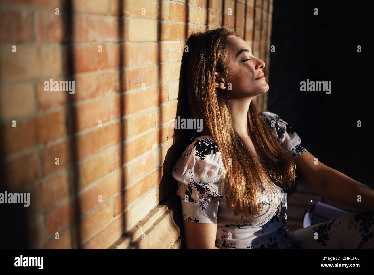 Primo piano di donna caucasica seduta a terra godendo la sensazione del calore del sole sul suo volto che entra dall'esterno Foto Stock