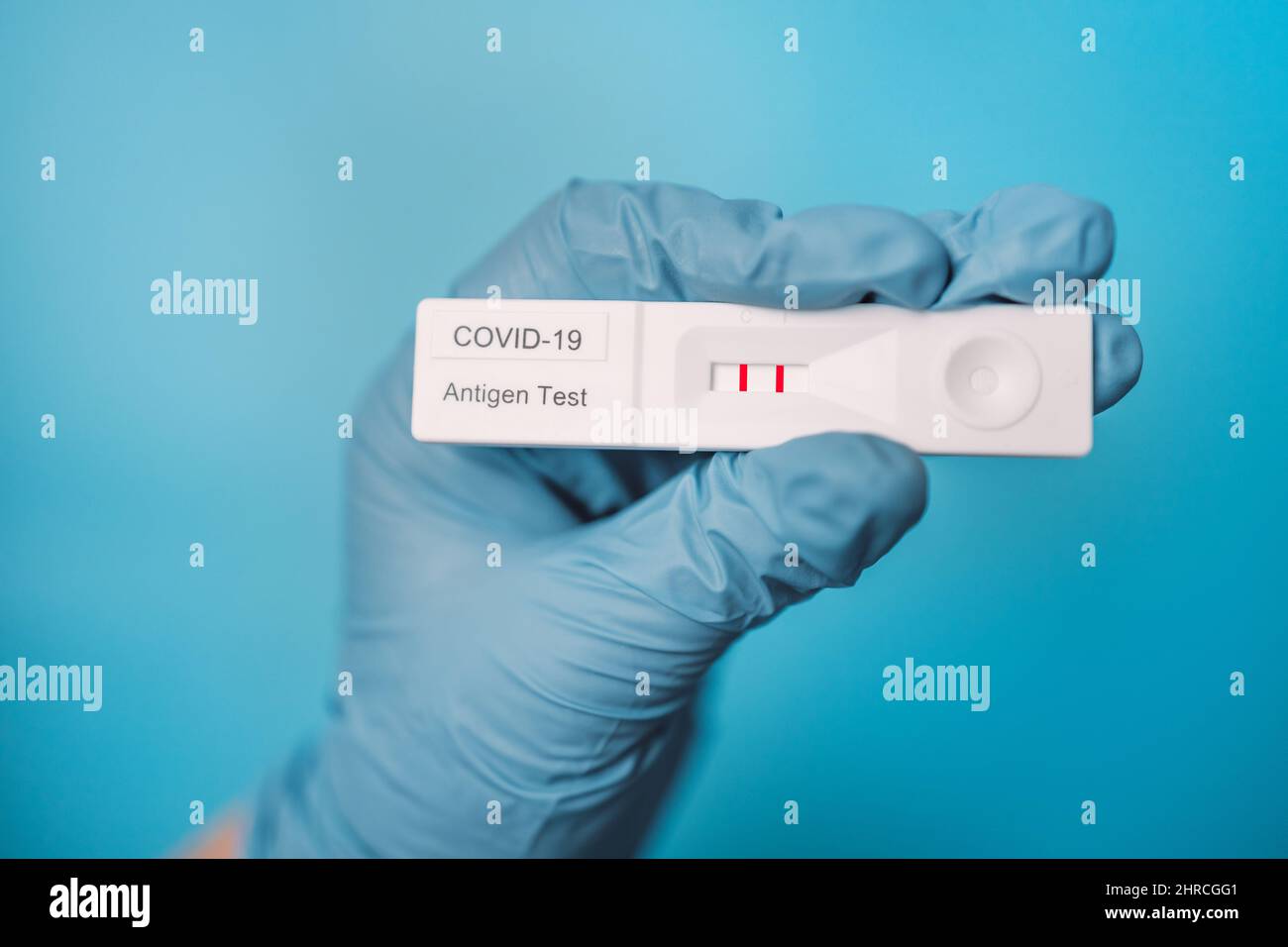 Primo piano del medico o dell'infermiere che tiene una mano positiva a flusso laterale rapido COVID 19 test su sfondo di colore blu chiaro Foto Stock